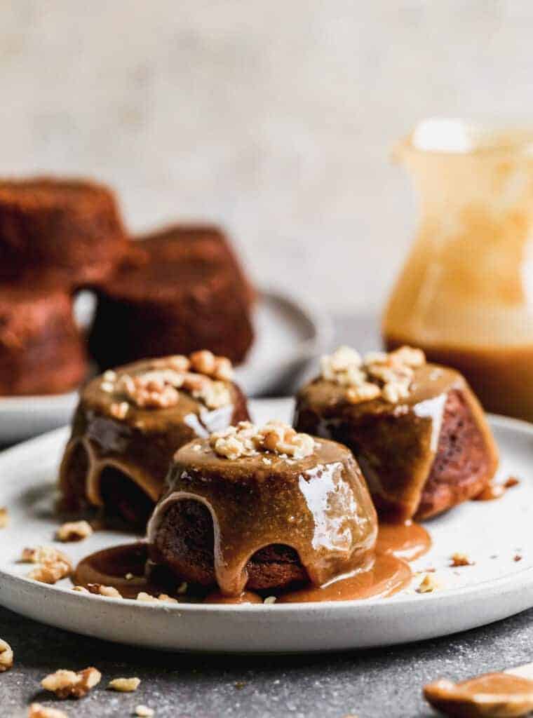 Three sticky toffee pudding cakes on a plate with sauce and crushed walnuts sprinkled on top.
