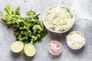 Toppings for pozole, including shredded cabbage, chopped onion, radishes, cilantro and limes.