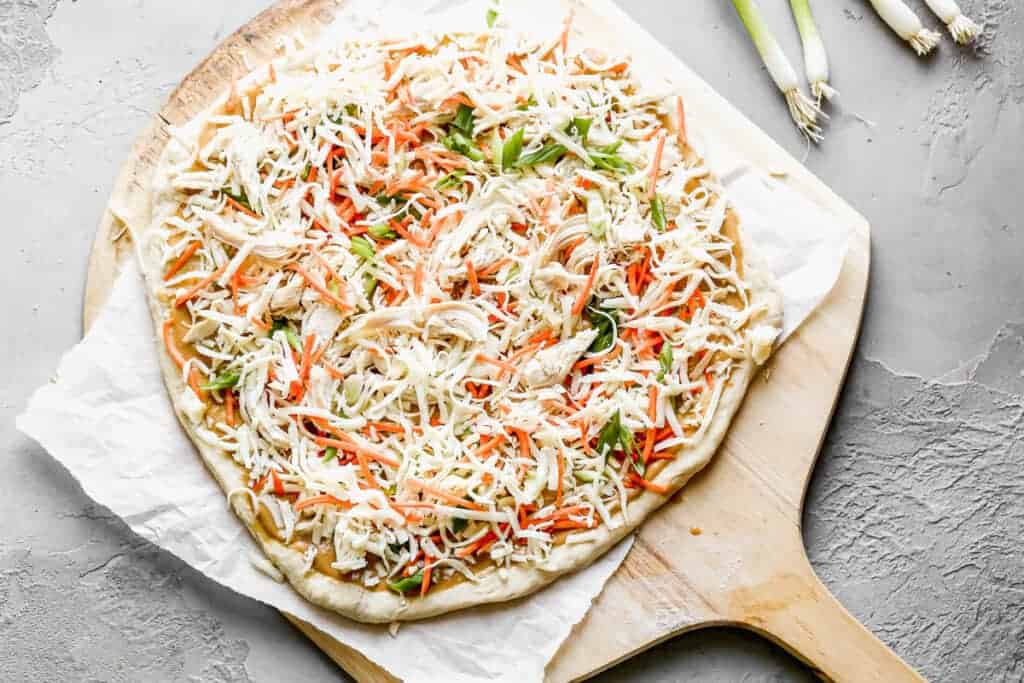 Toppings for Thai Chicken Pizza added to rolled out pizza crust dough, ready to bake.