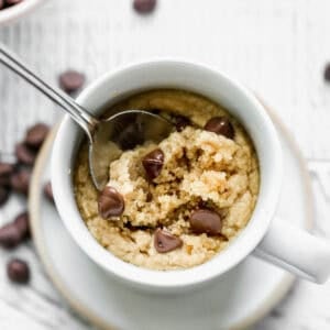 The best Peanut Butter Mug Cake recipe in a white mug with a few chocolate chips on top and a spoon scooping up a bite.