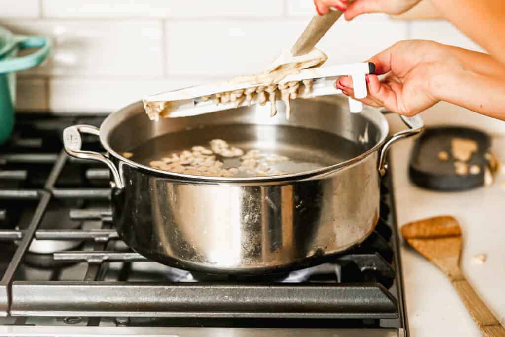 La pâte Spaetzle est poussée à travers les trous d'une râpe, dans une casserole d'eau bouillante.