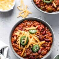 A bowl of Spicy Chili garnished with jalapeños and shredded cheddar cheese.