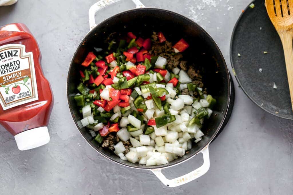 Browned ground beef, chopped onion and chopped bell peppers in a large pot.