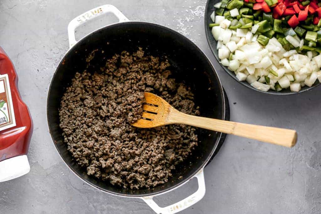 A pot with cooked ground beef and a wooden spoon in it.