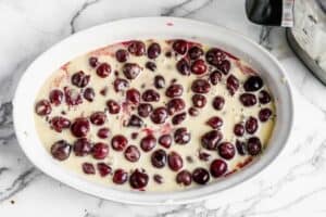 Cherries in a baking dish with clafoutis batter poured on top.