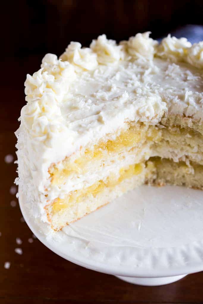 A whole coconut cake served on a cake stand, with a few slices removed to show the layers of cake and coconut frosting inside the cake.