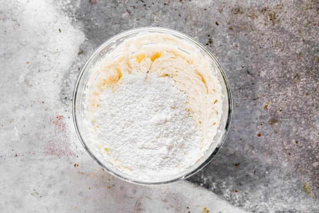 Fromage à la crème et beurre battus pour lisser dans un bol à mélanger et sucre en poudre ajouté sur le dessus.