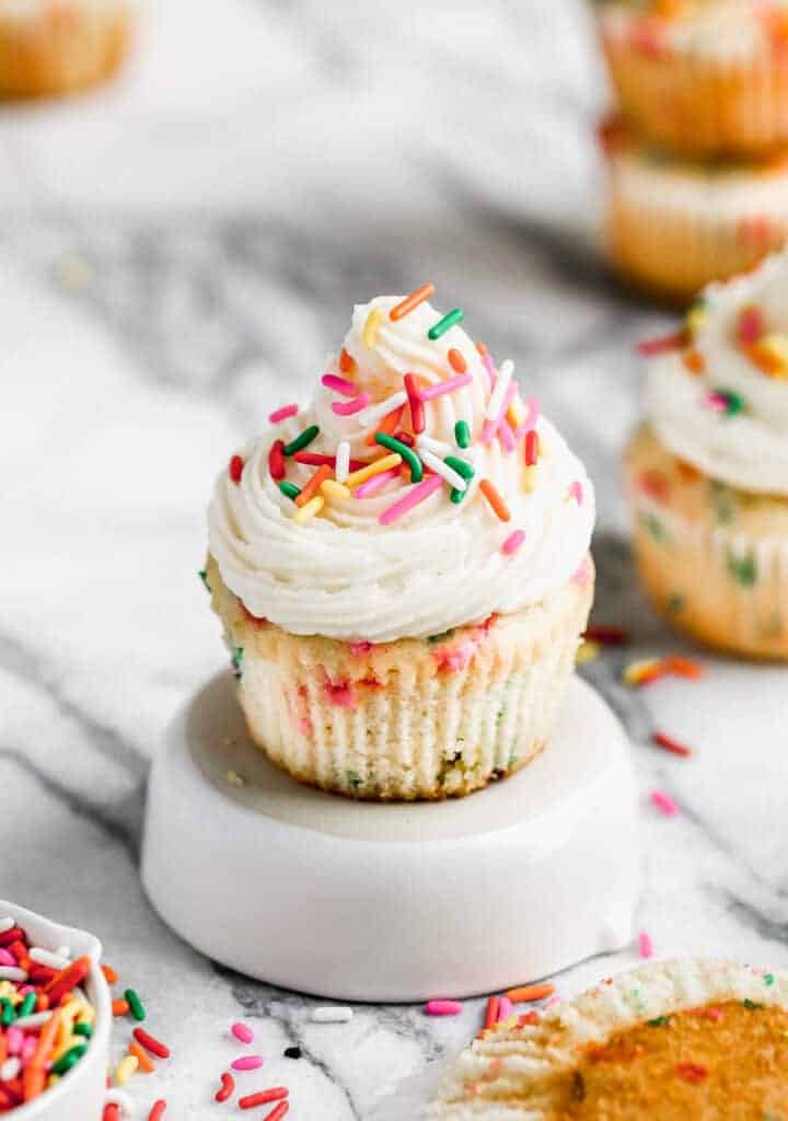 A homemade funfetti cupcake on a plate, with buttercream frosting and sprinkles on top.