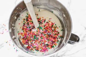 Cupcake batter in a mixing bowl with sprinkles added to it, to make funfetti cupcakes.