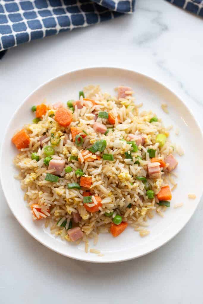 Ham fried rice with peas, carrots and ham, served on a white plate.