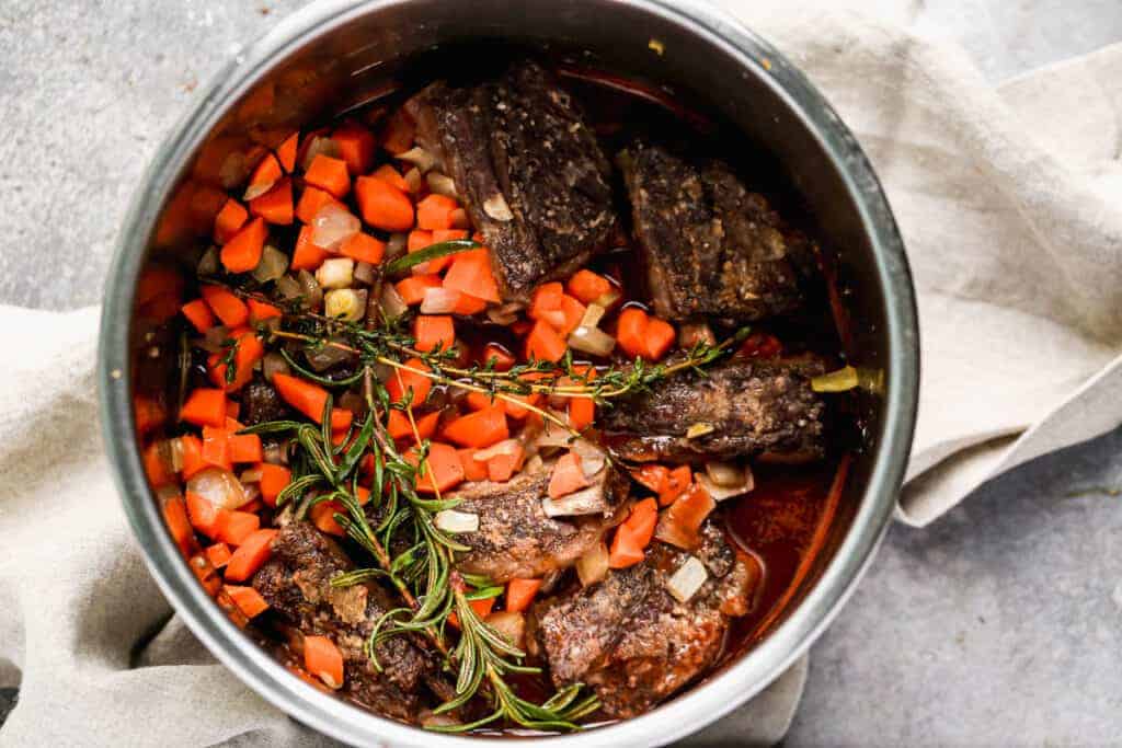 Beef short ribs, carrots, onion, herbs and liquid added to an instant pot and ready to pressure to cook.