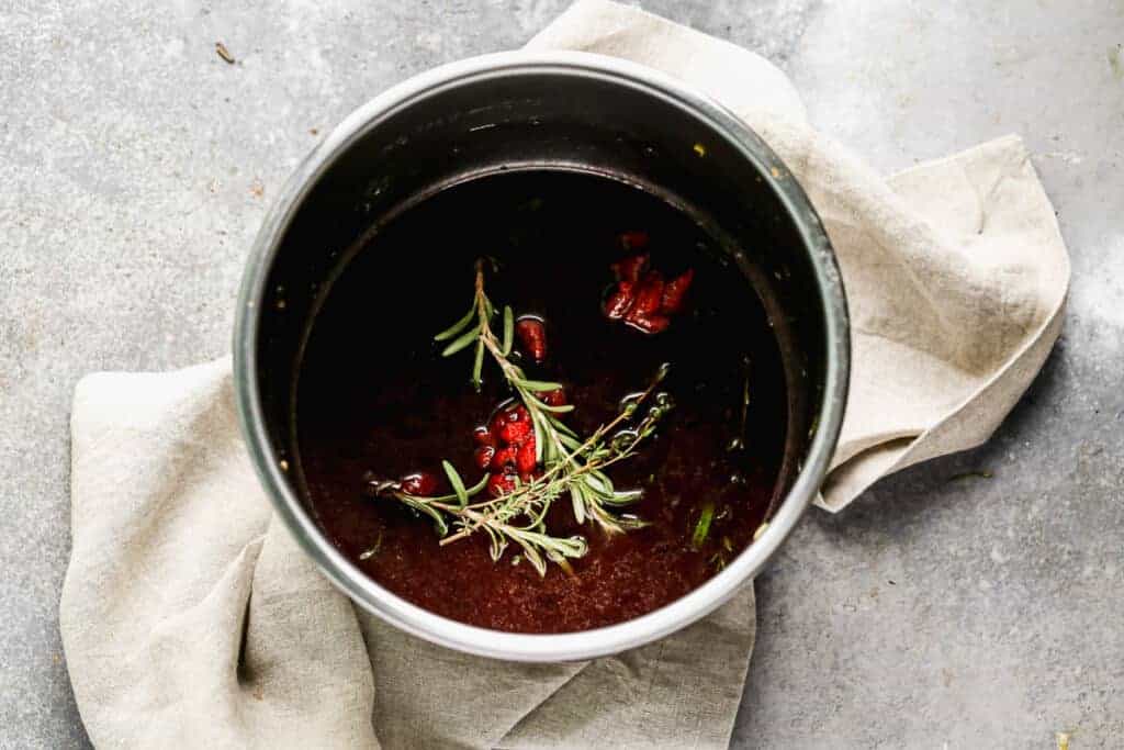 Beef broth, wine and herbs added to an instant pot to make instant pot short ribs.