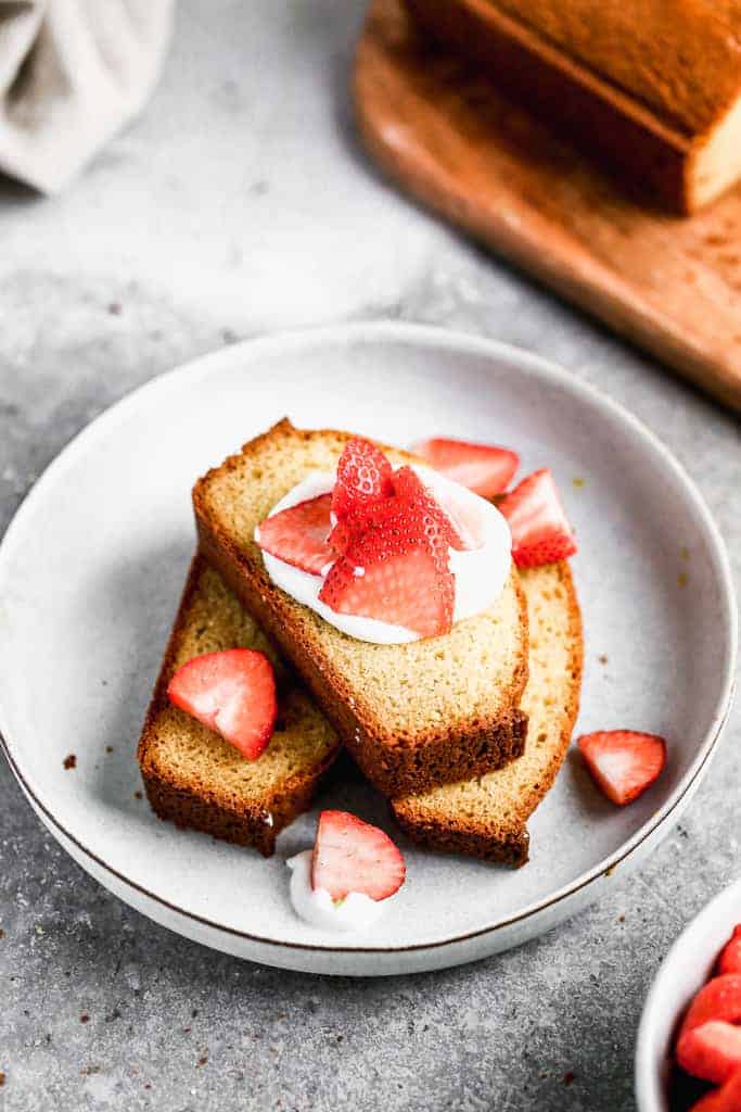 Three slices of Sour Cream Pound Cake on a plate with whipped cream and sliced strawberries on top.