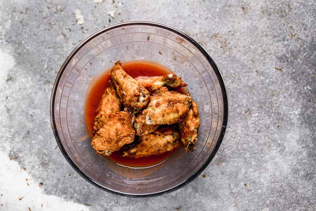 Cooked chicken wings tossed in wing sauce, in a bowl.
