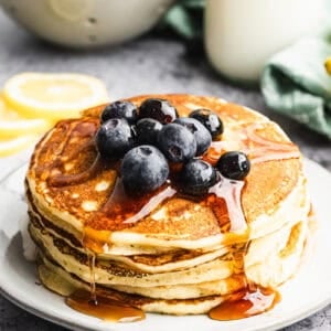 A stack of simple Lemon Ricotta Pancakes topped with fresh blueberries and drizzled with maple syrup.