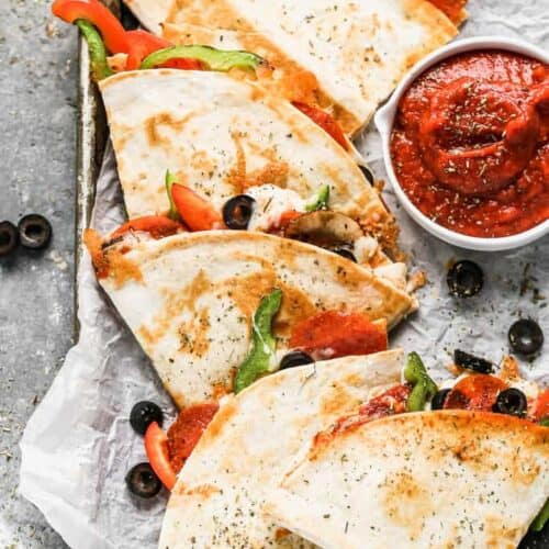 Pizza quesadillas on a baking sheet with a side of marinara sauce.