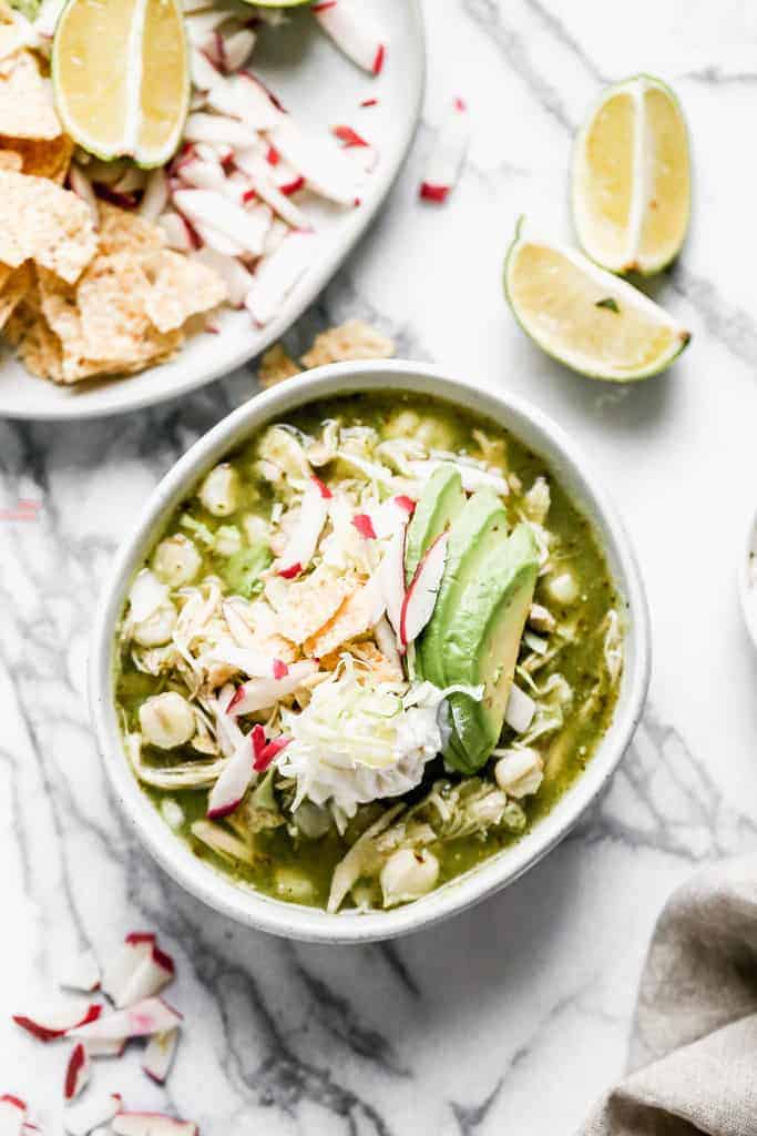 A bowl of Pozole Verde made with chicken, served with sliced avocado, cabbage and radishes, for garnish.