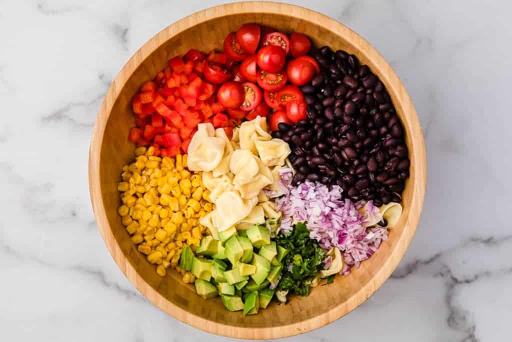 Cooked Tortellini, black beans, corn, chopped onion, avocado, cilantro, bell pepper and tomato in a bowl.