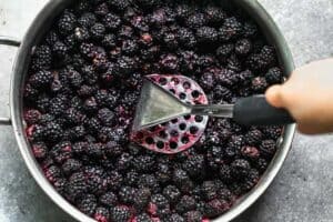 Blackberries in a pot being mashed with a potato masher.