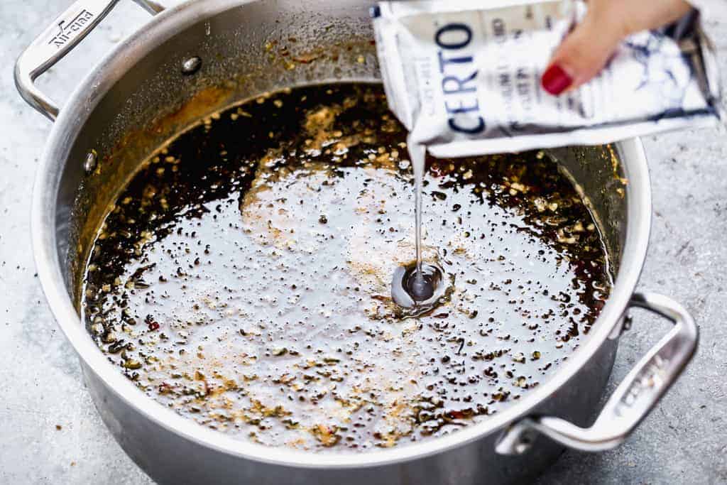 Liquid pectin being poured into a boiling pot of jalapeño jelly.