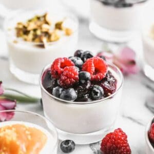 Panna Cotta in a cup with berry sauce and fresh berries on top.
