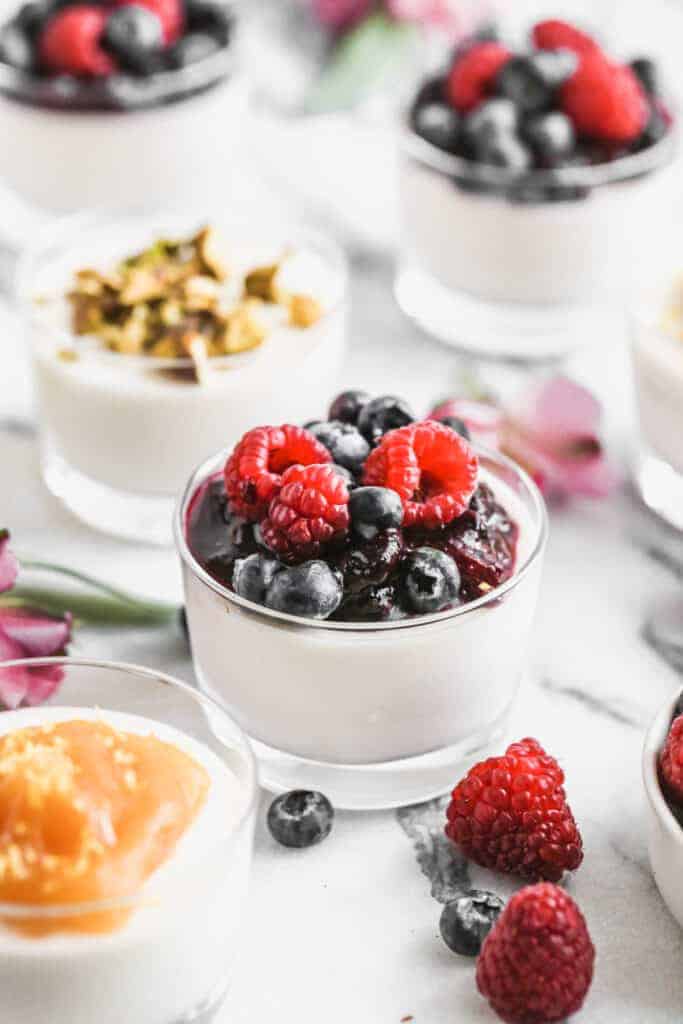 Panna Cotta in a cup with berry sauce and fresh berries on top.