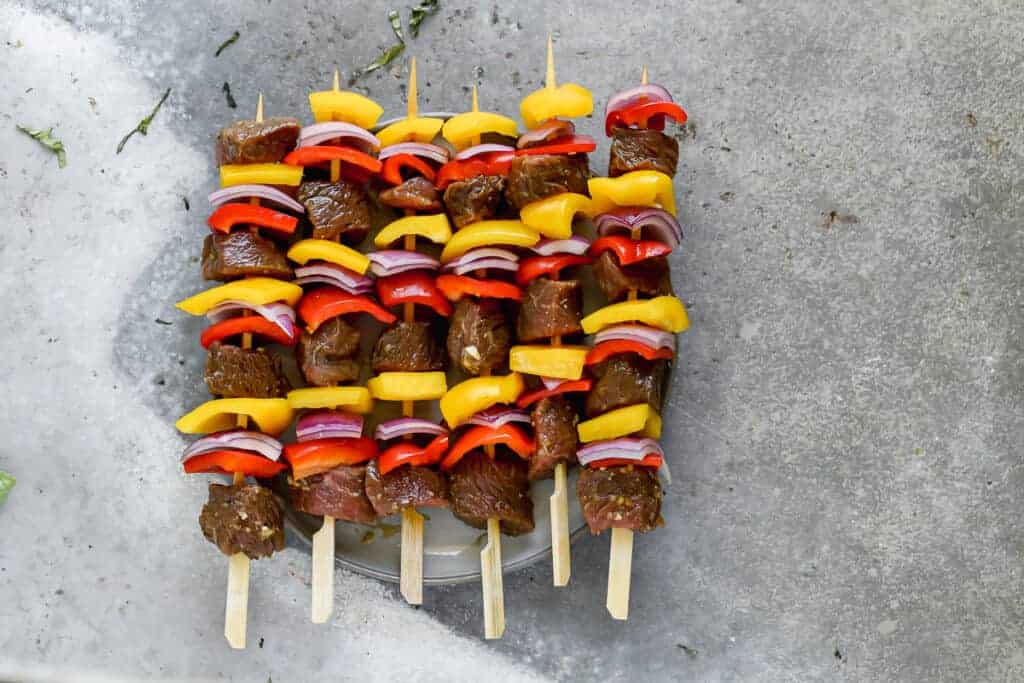 Uncooked, assembled steak kabobs on bamboo skewers with bell pepper and steak.