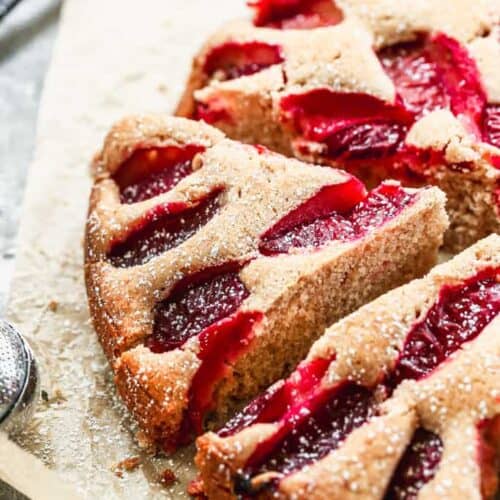 A baked plum cake with a slice cut from it.