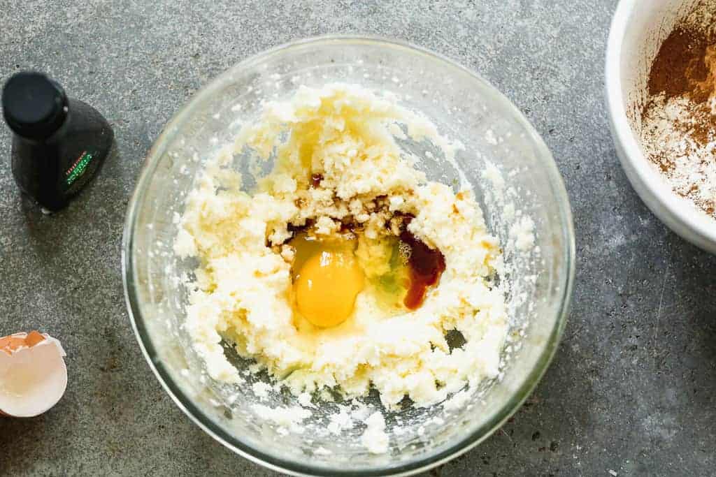 Un bol à mélanger avec du beurre en crème et du sucre et un œuf et des extraits ajoutés sur le dessus.