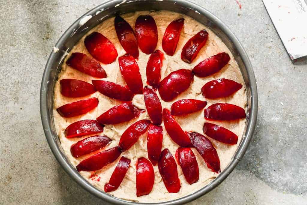 Plum cake batter in a springform pan with ripe sliced plums added on top.