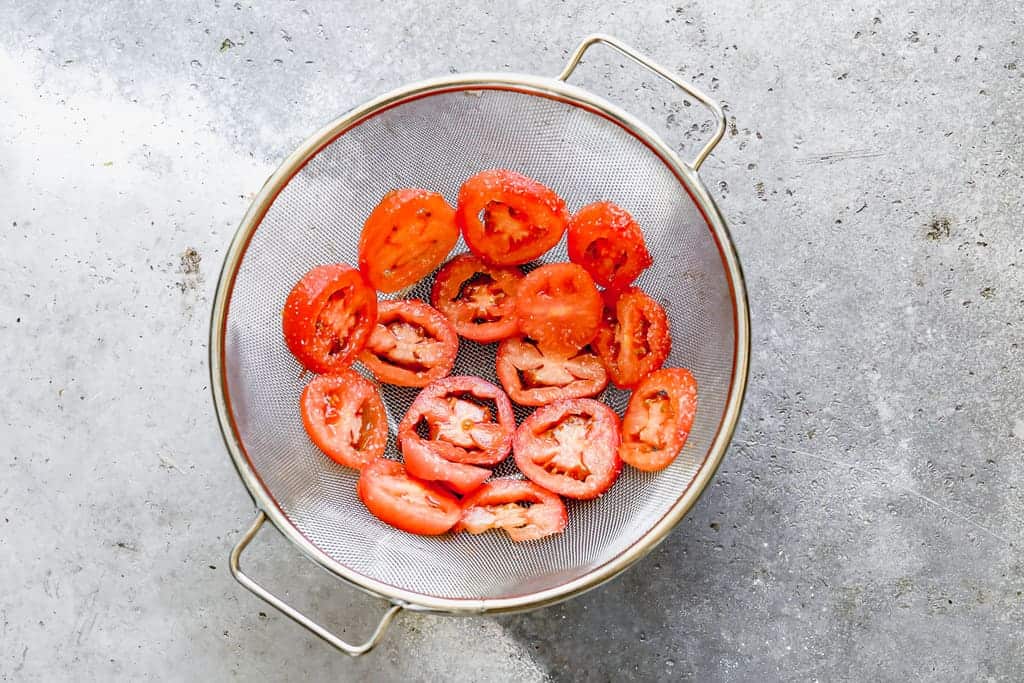 Sliced tomatoes in a fine mesh strainer.