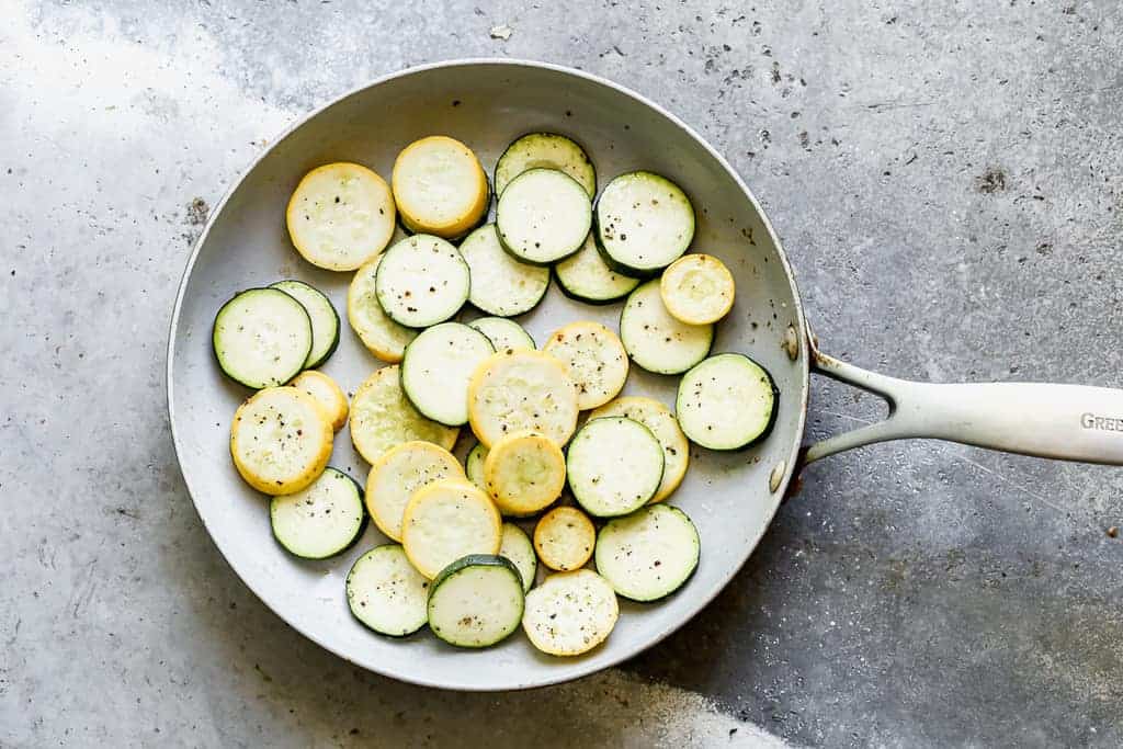 Sliced zucchini and yellow squash sautéing in a skillet.