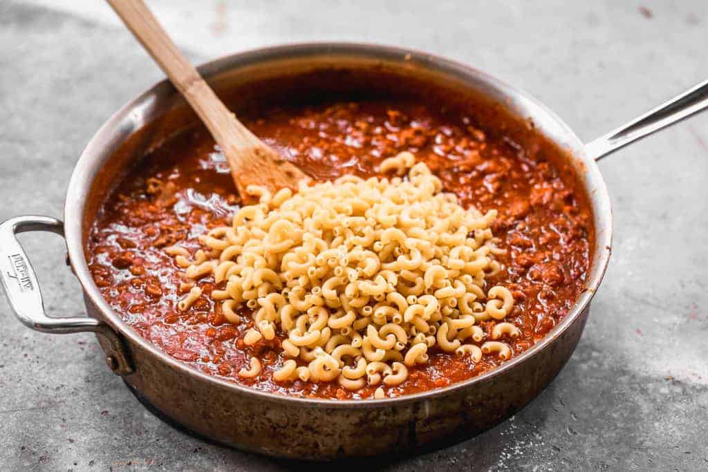 Dry elbow macaroni noodles added on top of meat sauce in a skillet.