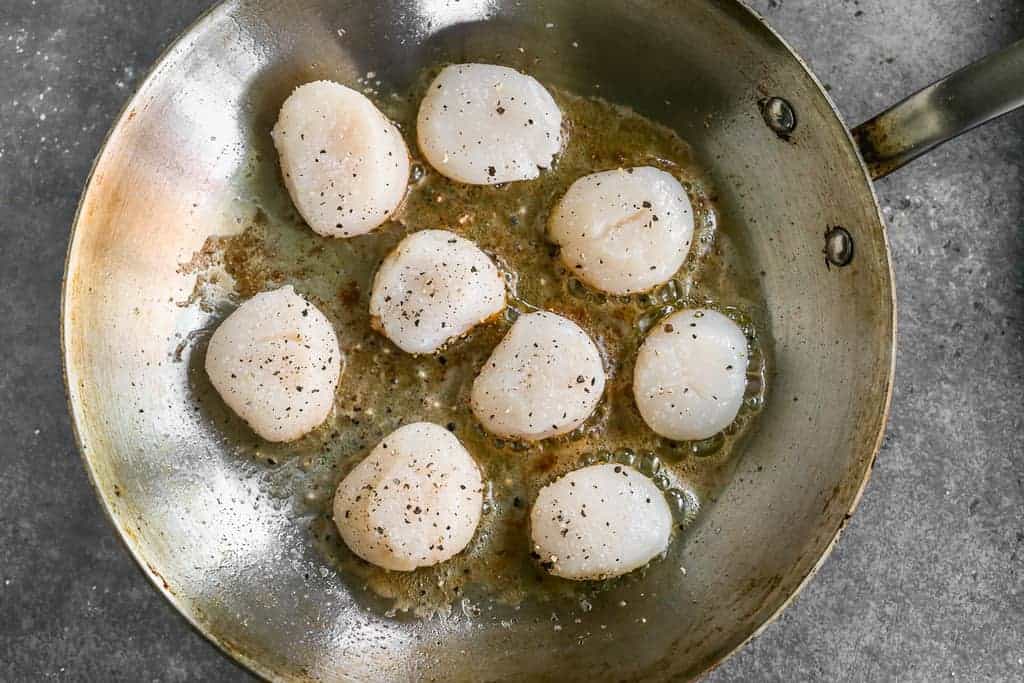 A saute pan scallops searing in hot butter and oil.