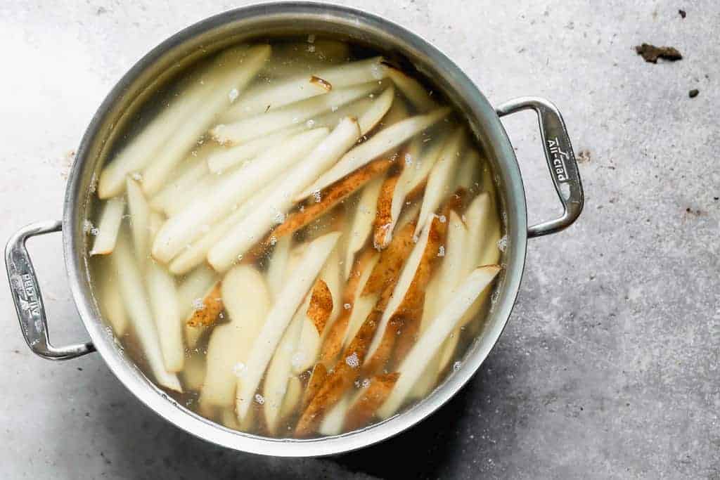 Sliced russet potatoes soaking in a pot of hot water, to prepare to make French Fries.