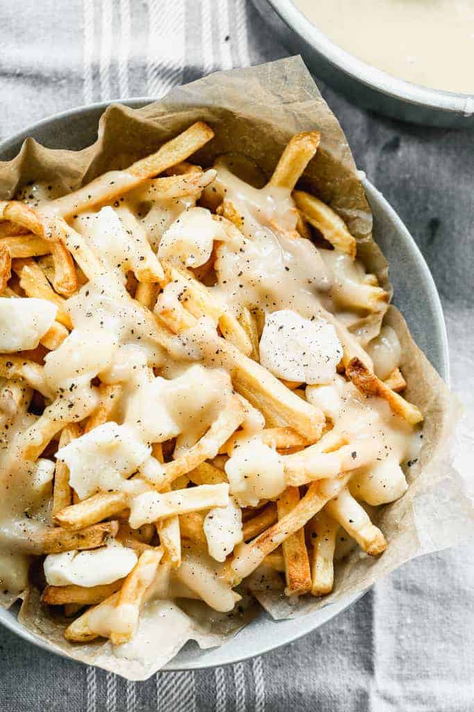 A bowl filled with Canadian Poutine, including fries topped with white cheese curd and gravy.