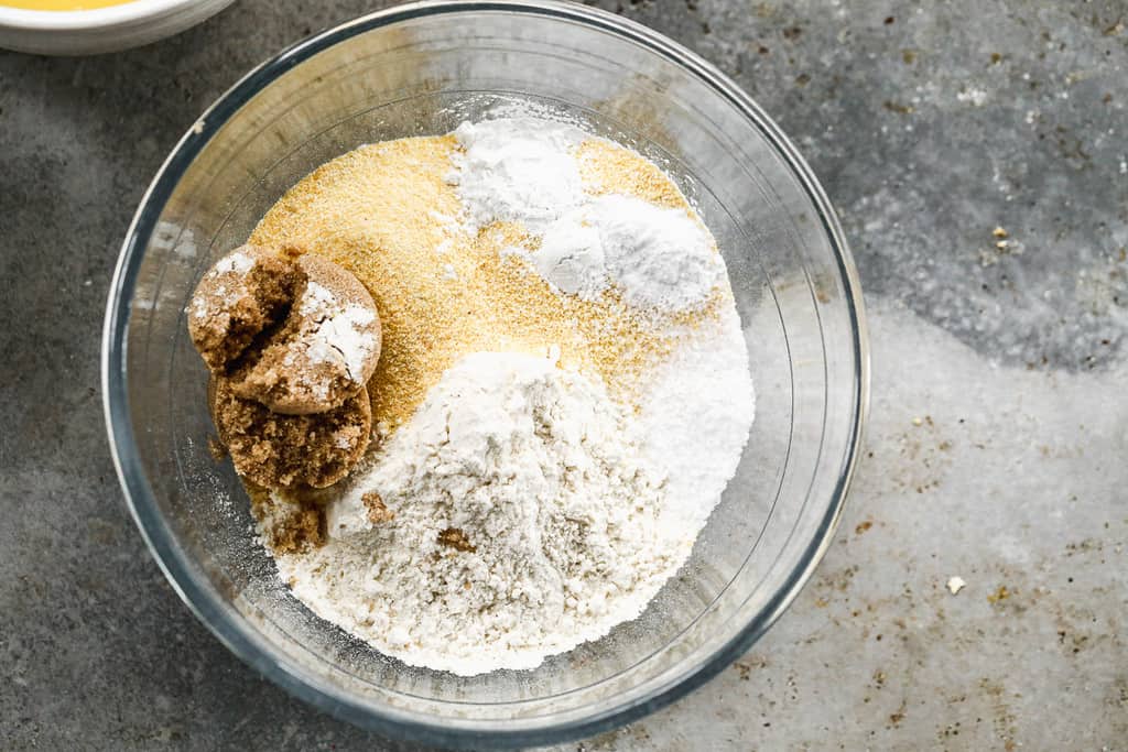 A mixing bowl with flour, cornmeal, brown sugar, salt, baking soda and baking powder in it.