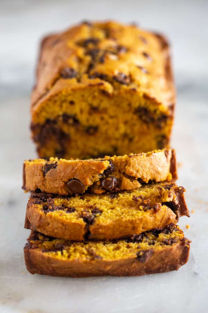 A loaf of pumpkin chocolate chip bread with three slices cut.