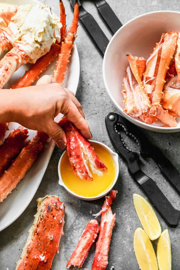 A hand dipping a piece of crab in melted butter.