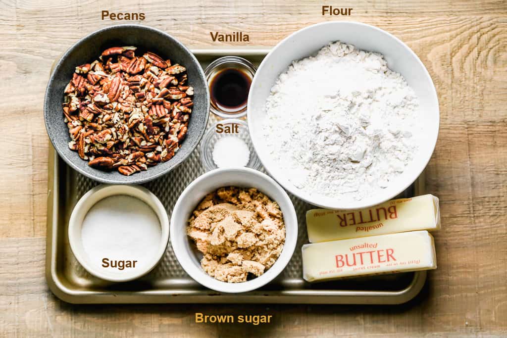 A cookie sheet with the ingredients to make pecan sandies, including peacns, butter, flour, sugar and brown sugar.