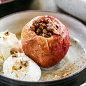 A warm baked apple on a plate with ice cream on the side.