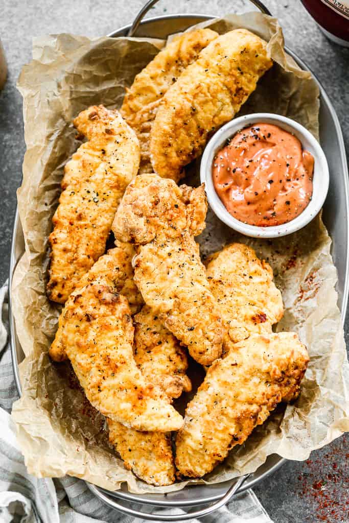Air Fryer Chicken Tenders served in a basket with dipping sauce. 