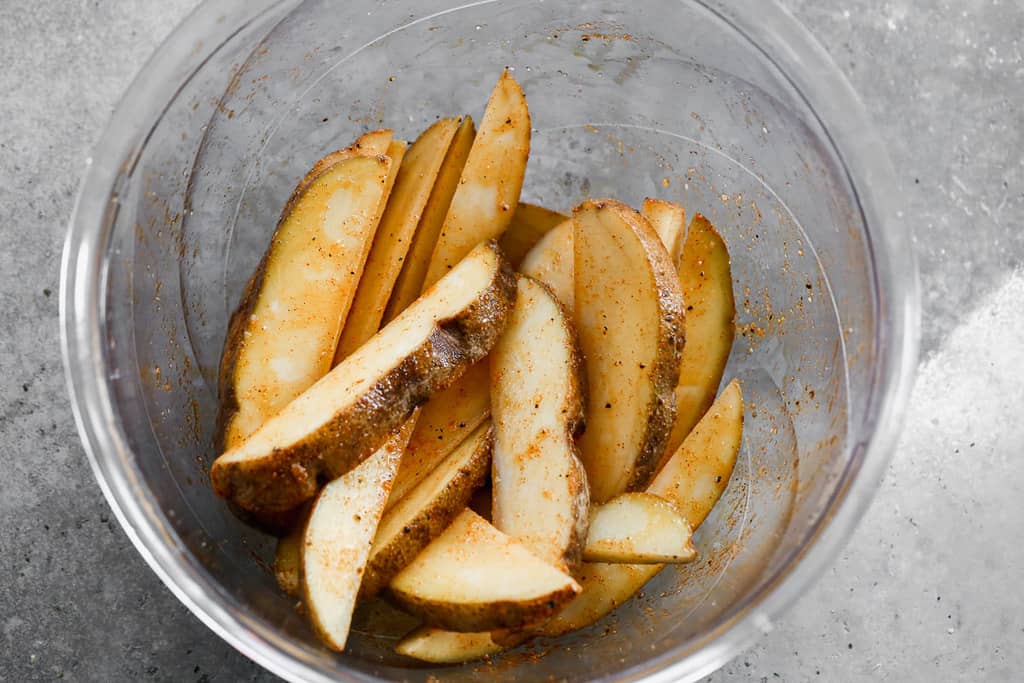 Potato wedges in a bowl, tossed in oil and seasonings.