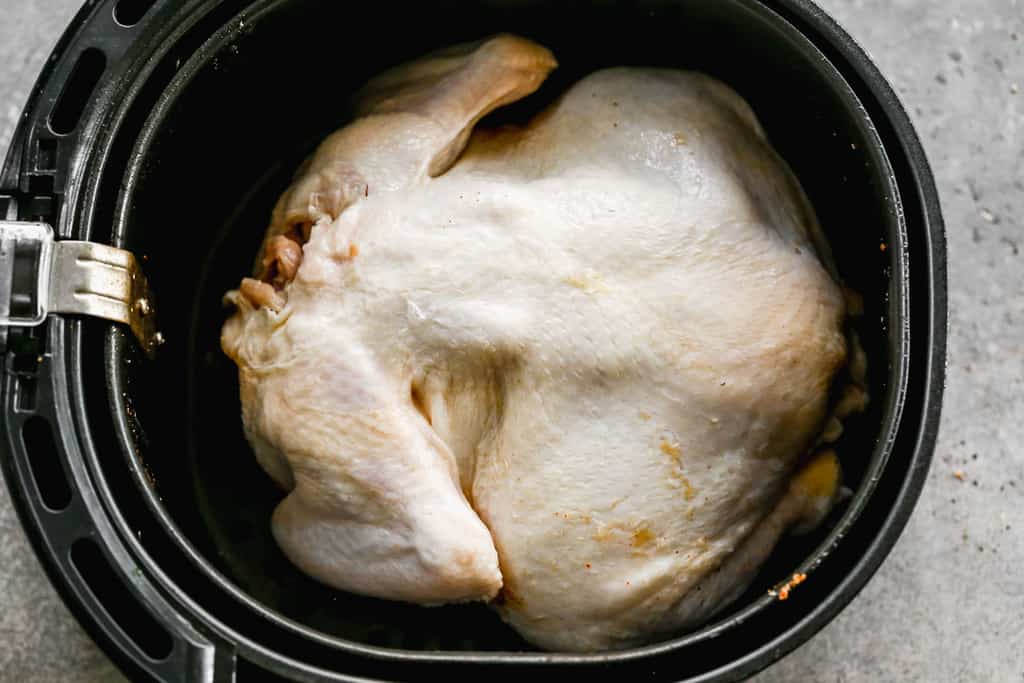 A whole chicken, placed breast-side down in an air fryer basket.