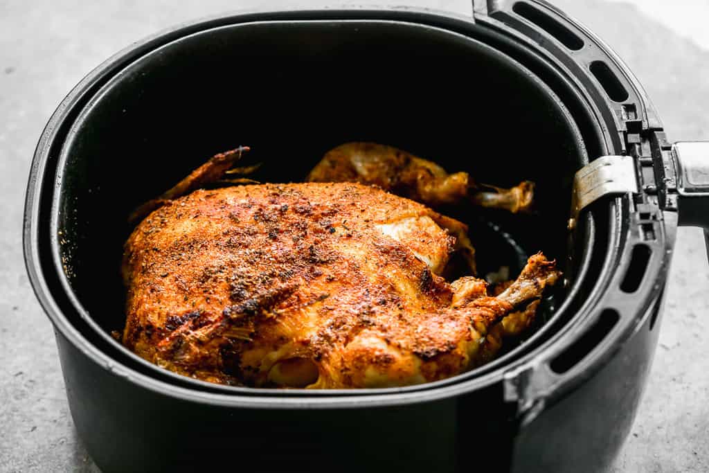 A whole chicken cooking in an air fryer, flipped to breast side up.