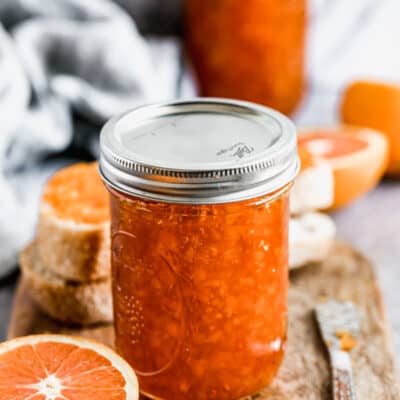 A jar of homemade orange marmalade, next to a fresh orange half.
