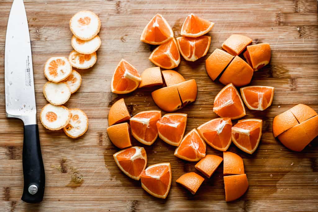 Quatre oranges fraîches sur une assiette, coupées en quartiers et hachées.