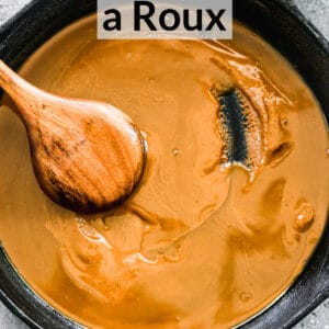 A homemade dark roux in a cast iron pan with a wooden spoon stirring it.