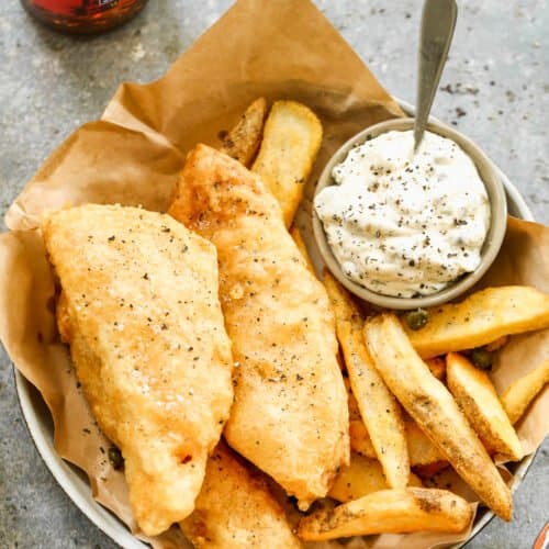 Homemade fish and chips in a basket with fries and tartar sauce.