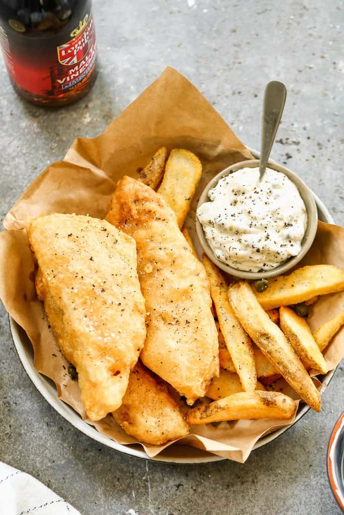 Homemade fish and chips in a basket with fries and tartar sauce.